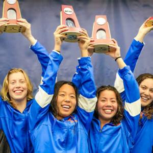 The Pomona-Pitzer women’s swim 和 dive team smile 和 hold up the NCAA trophies above their heads.